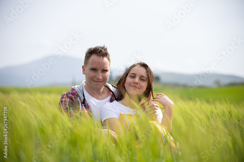 A young happy couple sitting on a green meadow with high grass