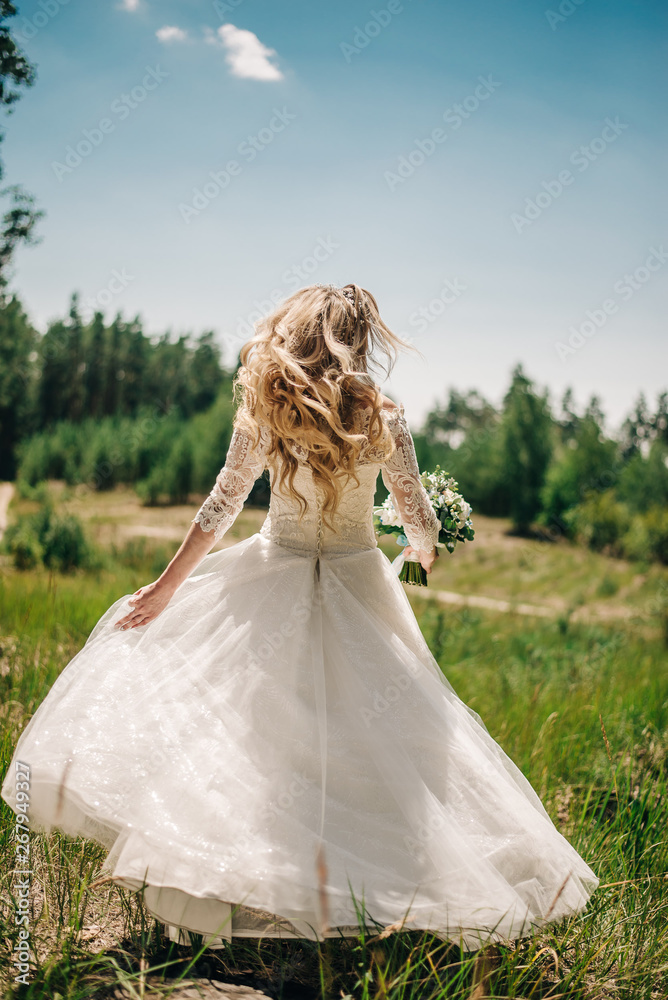 a bride in a white, magnificent dress is standing in a green field a bride in a white, magnificent dress is standing in a green field