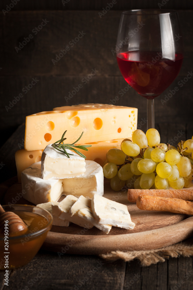 Cheese plate with brie, camambert, gauda with grapes,honey, crackers and nuts on a wooden background