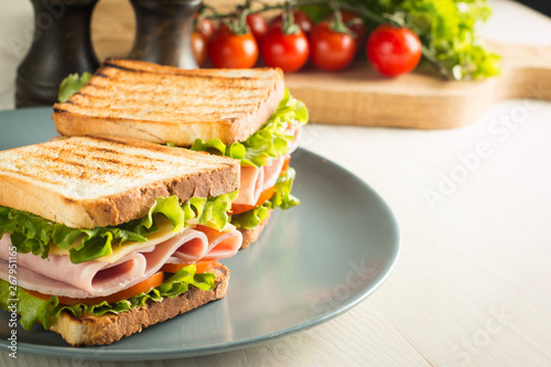 Close-up of two sandwiches with bacon, salami, prosciutto and fresh vegetables on rustic wooden cutting board. Club sandwich concept. photo