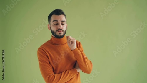 Portrait of thoughtful bearded man looking at camera on green background thinking over problem making decision touching beard. People and thoughts concept. photo