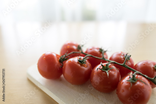 Tomaten an Rispe auf Holzbrett vor Fenster mit Gardine