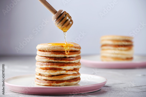 Stack of Pancakes with honey spoon and pouring honey on light background