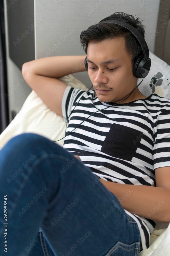 Fototapeta premium Young Malay guy looking at the phone relaxing at the bed
