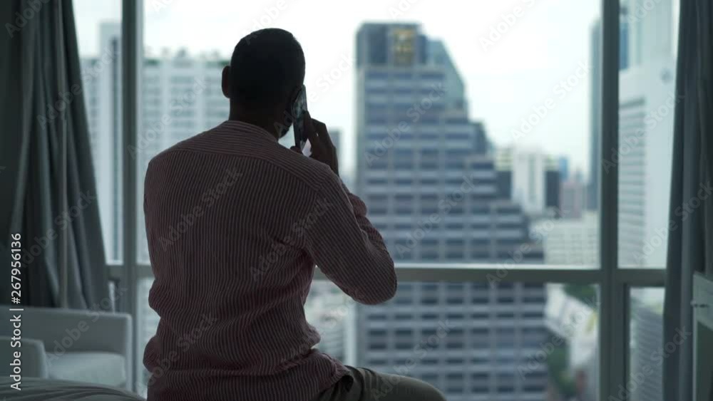 Young, happy man talking on cellphone sitting on bed at home