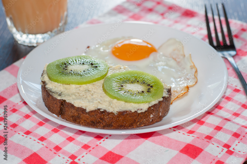 Healthy, tasty breakfast, juice, wholemeal bread sandwich with kiwi and a fried egg on white plate