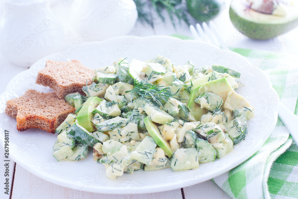 Salad with cucumbers, egg and avocado on a white plate, horizontal