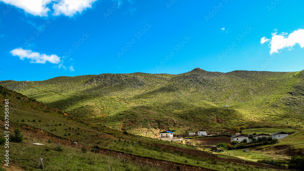 Green mountains with small village in a rural area on a clear blue sky day.