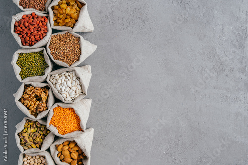 Small burlap sacks with almond, chickpeas, walnuts, buckwheat, raisins, goji against grey background with copy space for your advert photo