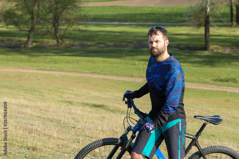 Cyclist in shorts and jersey on a modern carbon hardtail bike with an air suspension fork rides off-road on green hills near the forest Cyclist in shorts and jersey on a modern carbon hardtail bike with an air suspension fork rides off-road on green hills near the forest