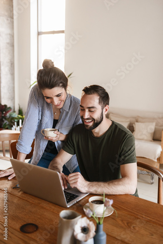 Image of candid brunette couple working on laptop together while sitting at table at home