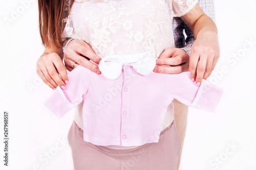 young couple expecting a baby. young parents. Male hands hold a pregnant belly. parental hands hold baby clothes. pink baby blouse. hands in the shape of a heart. waiting for a miracle. © Stanislav