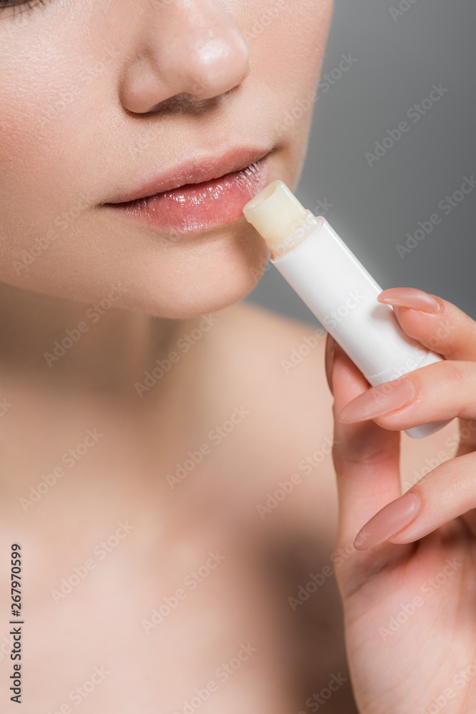cropped view of girl holding lip balm near lips isolated on grey cropped view of girl holding lip balm near lips isolated on grey