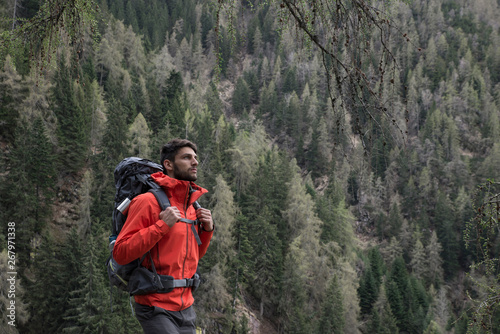 Portrait of an athletic healthy man hiking in nature and looking the at the view. High mountain fir forest background.