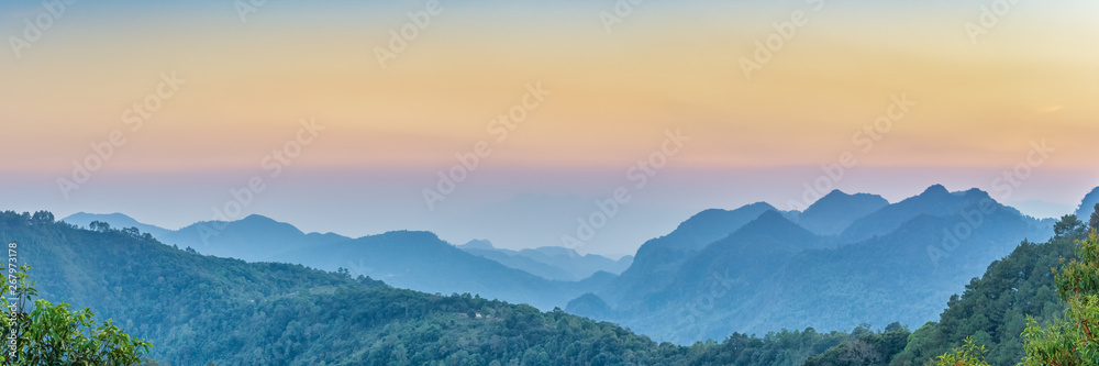 Nature Web Banner. Mountain view sunset panorama view of many hill and green forest cover with soft mist with colorful sky background, sunset at  Doi Ang Khang, Chiang Mai, Thailand.