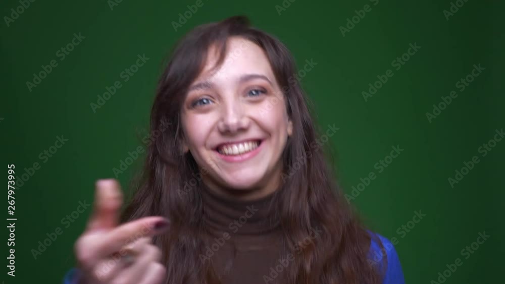 Young brunette businesswoman smiles joyfully into camera and points finger into it on green background. Young brunette businesswoman smiles joyfully into camera and points finger into it on green background.