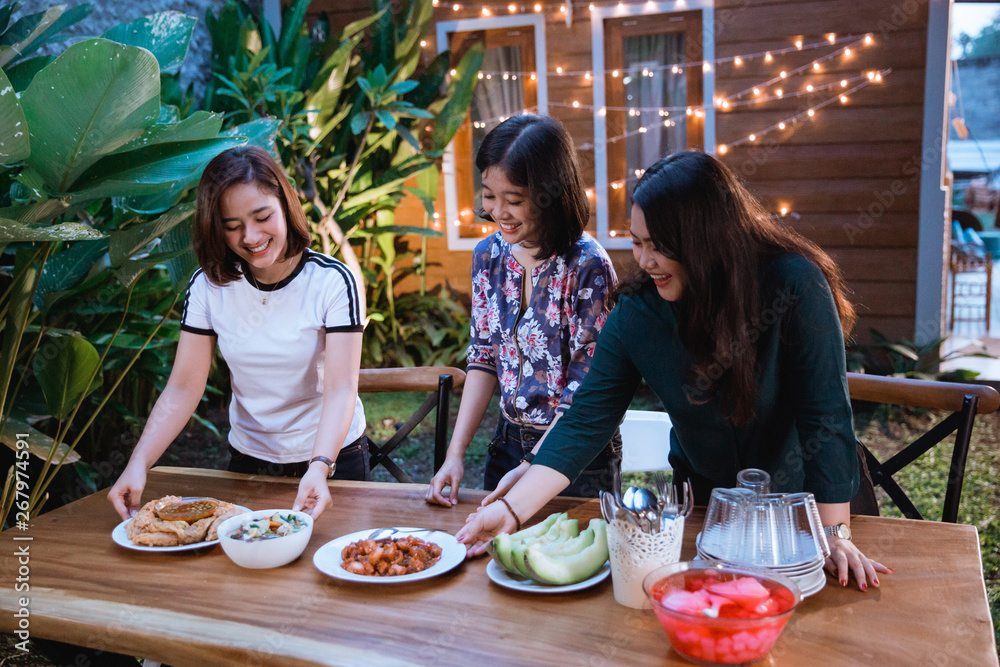 three woman preparing table for dinner at home backyard garden party