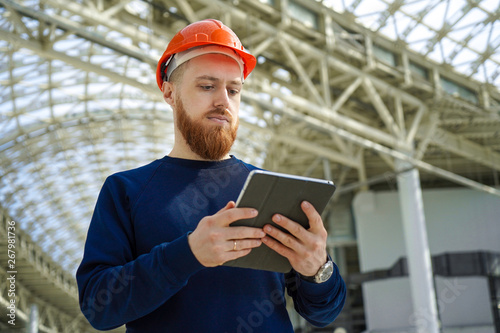 The average plan portrait of an adult man in a helmet looks into the tablet personal computer, horizontal, space for free signature