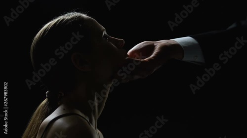 Man raising head of submissive woman up against black background, sexual slavery photo