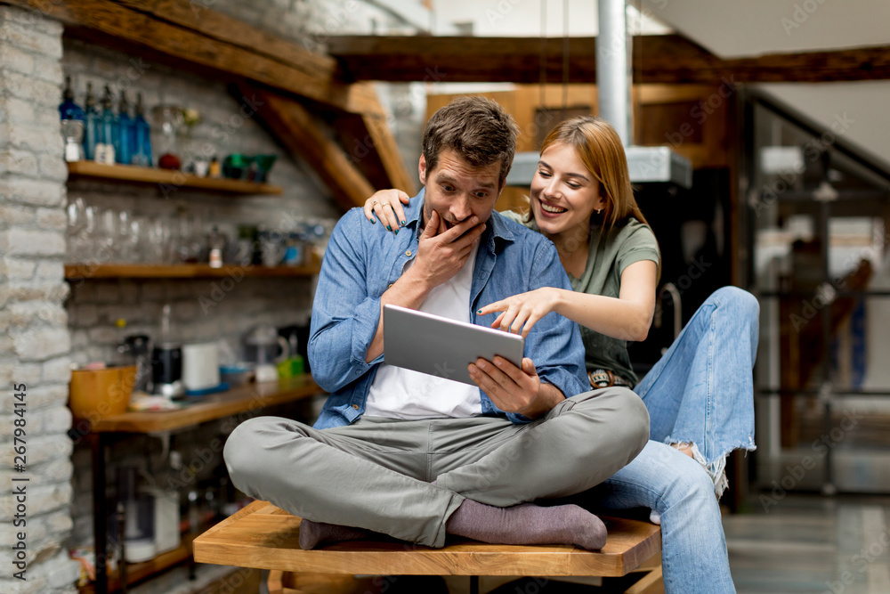 Young couple is using a digital tablet and smiling in kitchen at home Young couple is using a digital tablet and smiling in kitchen at home
