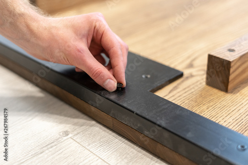 Man using screw fasten metal element on wooden table top