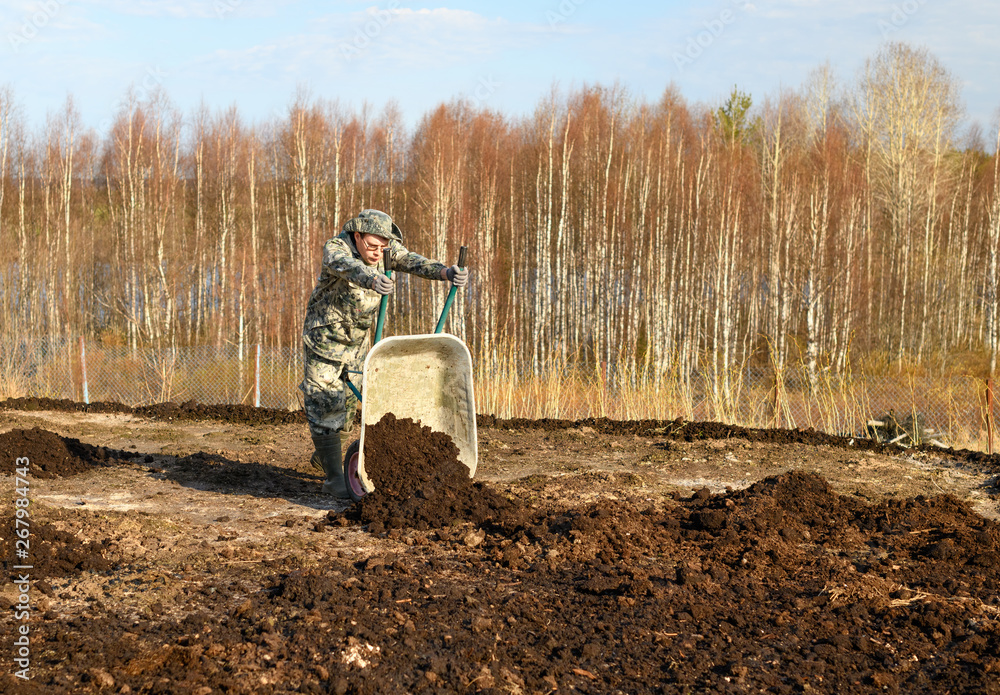 The man is unloading the peat from the wheelbarrow on the field in outdoors. The man is unloading the peat from the wheelbarrow on the field in outdoors.
