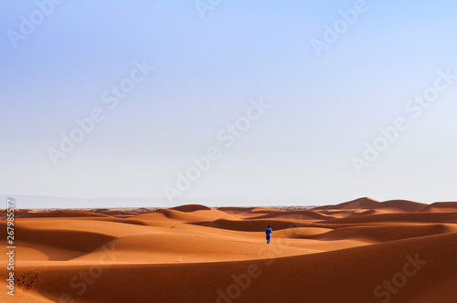 A person walks through sand dunes in the Sahara   A person in traditional clothing walks through the sand dunes in the Sahara  Morocco  Africa.
