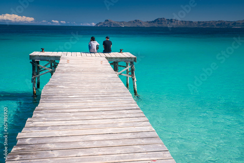 Man and woman sitting together on the pier in beautiful tropical sea. Playa de Muro, Spain.