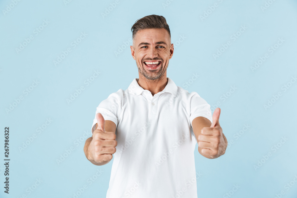 Fototapeta premium Handsome excited emotional adult man posing isolated over blue wall background showing thumbs up.
