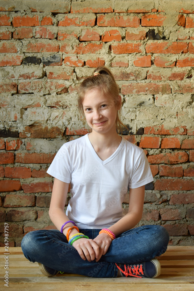 Young girl in jeans and white T-shirt is sitting on the floor and smiling. Concept portrait of a pleasant friendly happy teenager Young girl in jeans and white T-shirt is sitting on the floor and smiling. Concept portrait of a pleasant friendly happy teenager