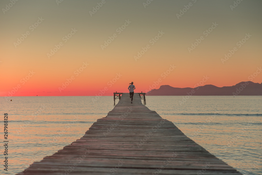 Woman running on wooden pier. Sunrise sea landscape in background