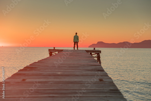 Man standing alone on the pier. Summer sunset sky in background.