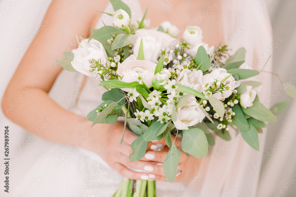 bride's hands hold beautiful bridal bouquet of white roses.