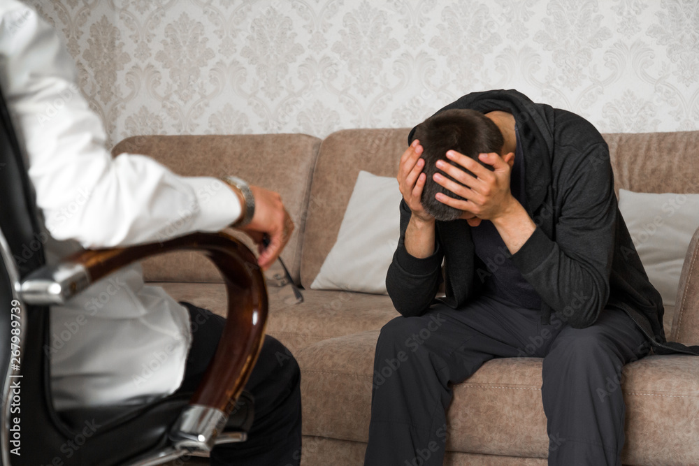 young man is sitting on couch and covers face with hands in the psychologist office young man is sitting on couch and covers face with hands in the psychologist office