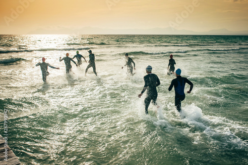 Start of a triathlon. Silhouette of competitors in wet suits, who running into the water