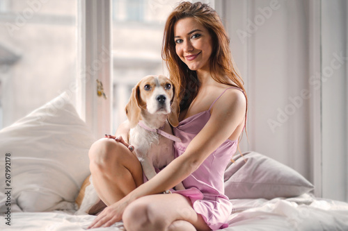Young pretty woman wearing lingerie and sitting in bed with her dog.