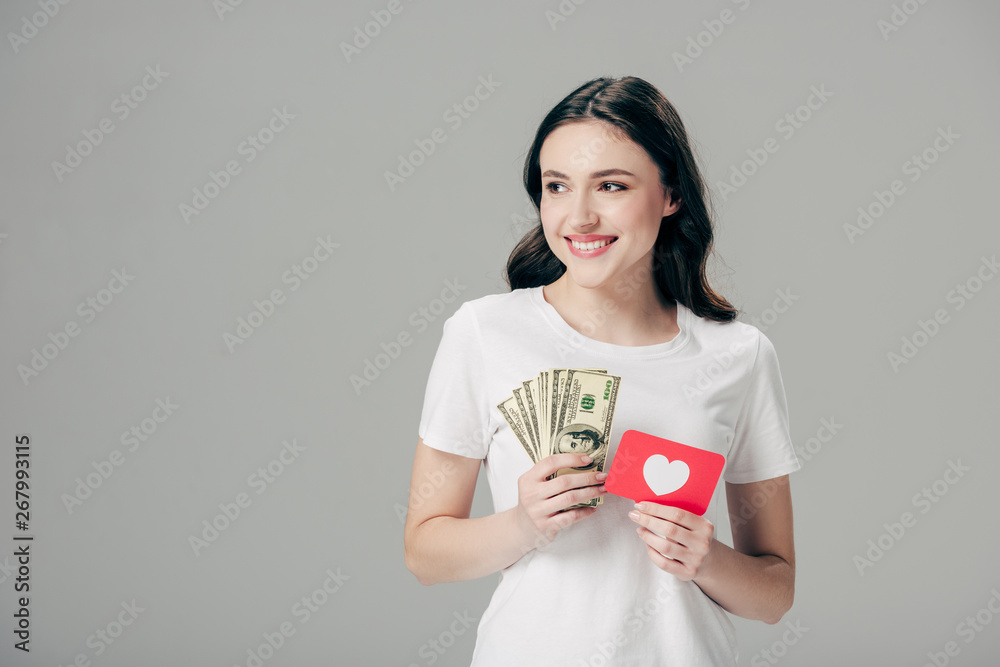beautiful smiling girl holding dollar banknotes and red paper cut card with heart symbol isolated on grey beautiful smiling girl holding dollar banknotes and red paper cut card with heart symbol isolated on grey