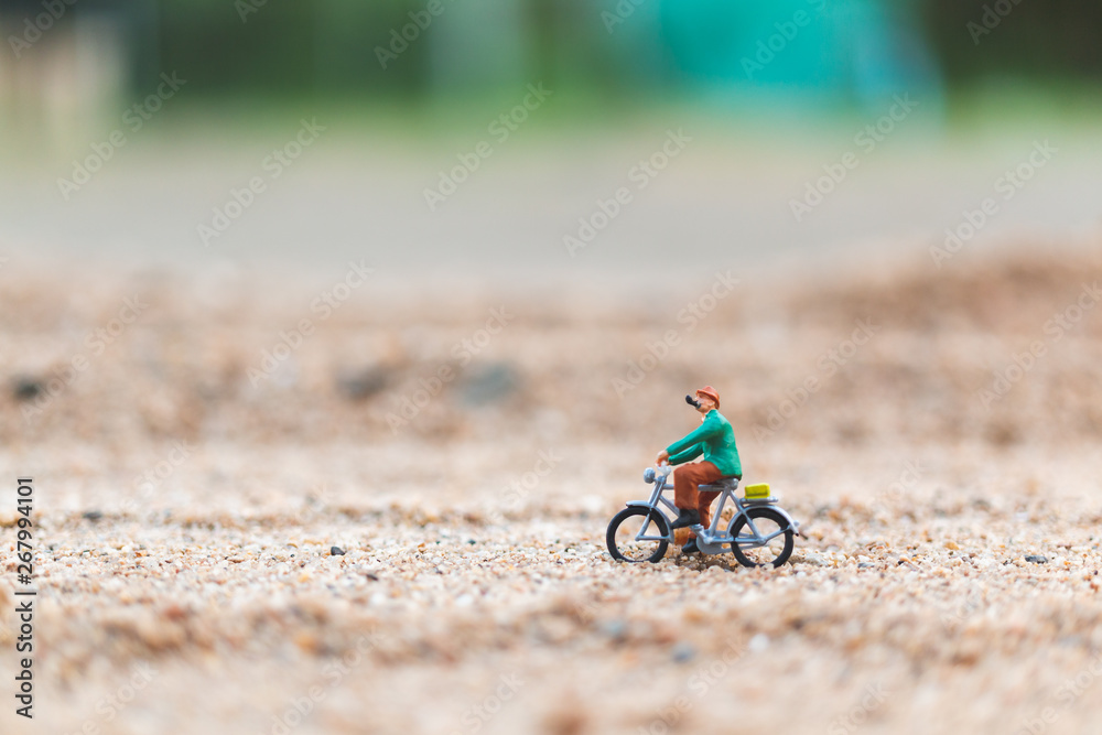 Miniature people : Travellers riding a bicycle  on The sand