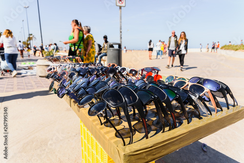 Valencia, Spain - May 12, 2019: Illegal immigrants selling false glasses and souvenirs to tourists on the beach of Valencia. photo