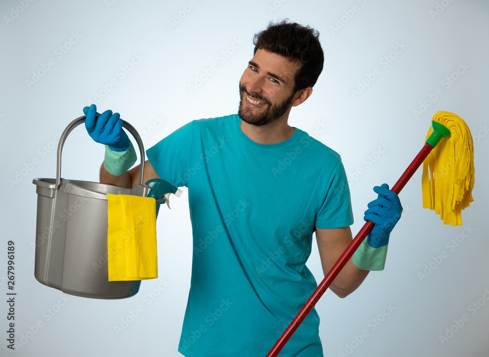 Young attractive man holding cleaning tools and products in bucket isolated in blue background Young attractive man holding cleaning tools and products in bucket isolated in blue background