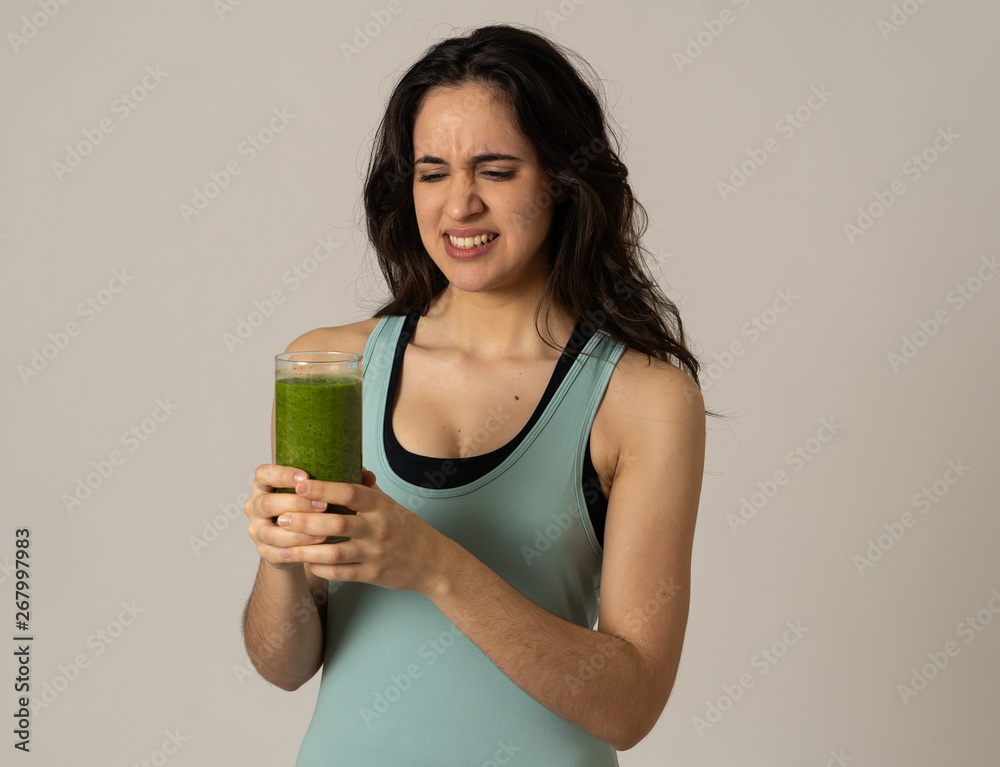 Beautiful young sports latin woman boring of diet holding green smoothie in dislike Beautiful young sports latin woman boring of diet holding green smoothie in dislike