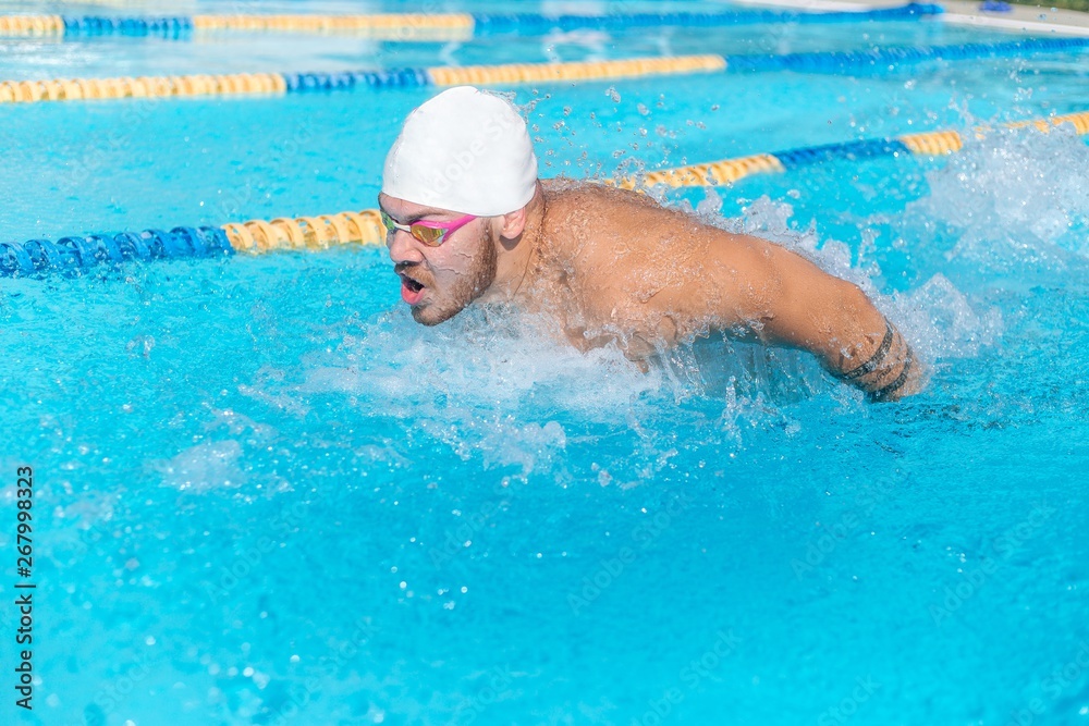 Swimmer in underwater glasses and a swimming cap swims in the pool brace