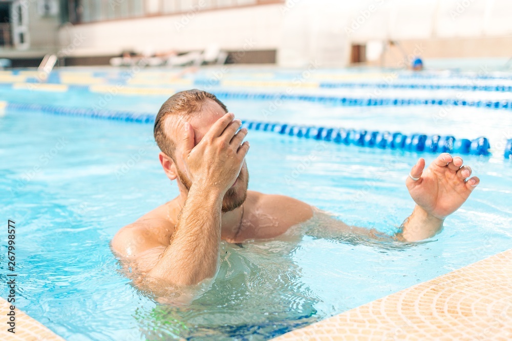 Muscular male swimmer in outdoor pool wipes her face from the water