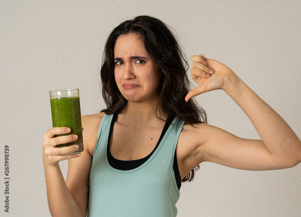 Beautiful young sports latin woman boring of diet holding green smoothie in dislike Beautiful young sports latin woman boring of diet holding green smoothie in dislike
