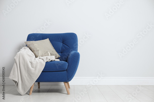 Stylish armchair with pillow and plaid near white wall, space for text. Interior design