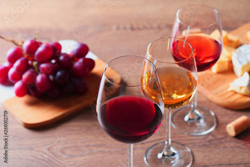 Glasses with different wines and appetizers on wooden table, closeup. Space for text