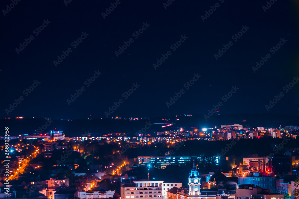 Fototapeta premium Landscape of city at nighttime with buildings and streets in a blue and violet neon light - Top scene of a town with modern architecture – Concept image for night life and travel