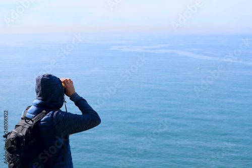 Traveler with a backpack by the sea looks through binoculars