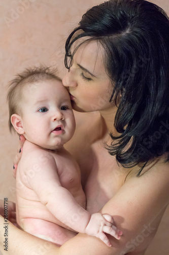 Young beautiful mother brunette without clothes holding her arms and kissing her little son
