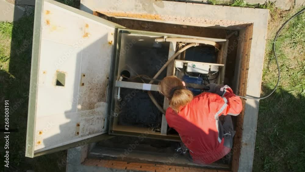 female cleaner washes a septic tank using a high pressure car wash. top view. Maintenance of biological water treatment plant in spring.